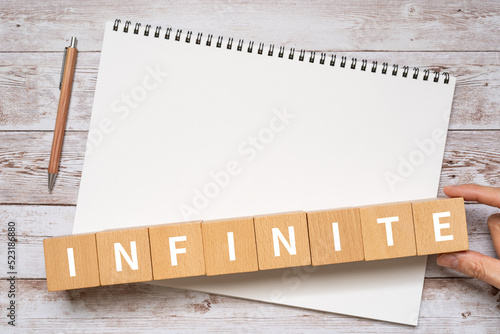 無数・無限・空間のイメージ｜「INFINITE」と書かれたブロック、ノート、ペン、手 