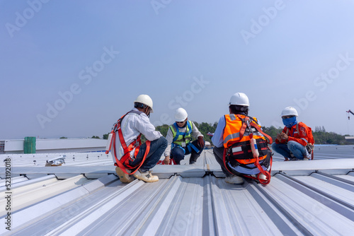 Team engineers wearing full safety body harness working on roof top for inspection metal roof sheet in large warehouse