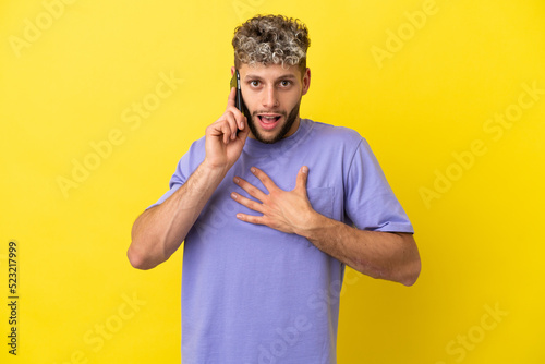 Young caucasian man using mobile phone isolated on yellow background surprised and shocked while looking right