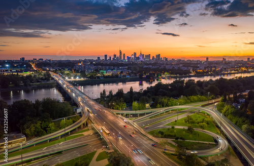Stunning sunset skyline, aerial view Warsaw, Poland. Drone shot of city downtown business center skyscrapers in background. Highway bridge over river and driving cars, amazing cloudscape evening dusk