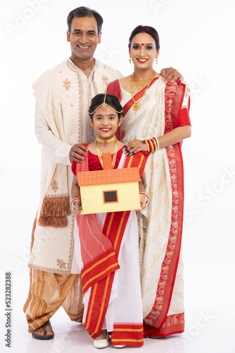 Happy bengali parents with girl holding model house in traditional clothing 