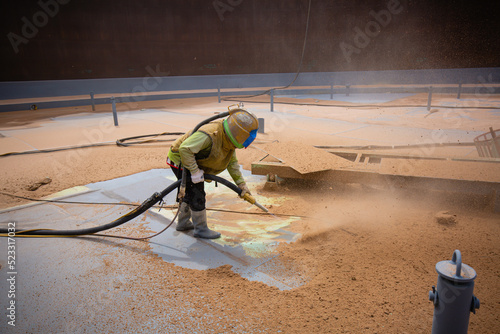 Male worker surface corrosion plate preparation by sandblasting bounce off of tank top deck.