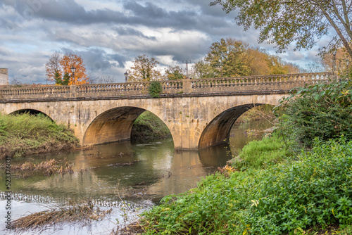 A view of the Melksham Town Bridge looking up river on an autumn day. The bridge on Bath Road crosses the River Avon and is a grade 2 listed structure of ashlar with arches and a balustraded parapet