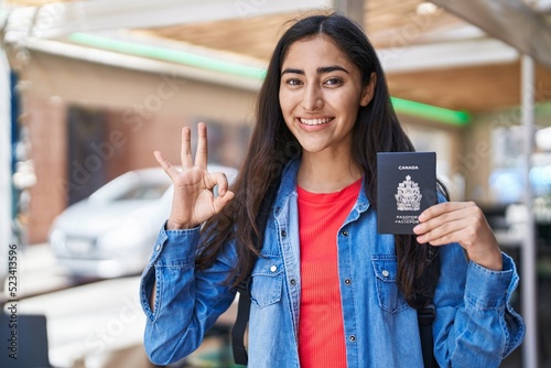 Young teenager girl holding canada passport doing ok sign with fingers, smiling friendly gesturing excellent symbol