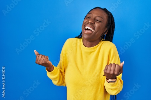 Beautiful black woman standing over blue background celebrating surprised and amazed for success with arms raised and eyes closed. winner concept.