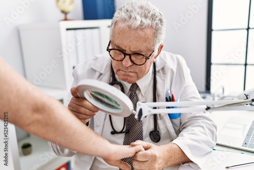 Middle age grey-haired man wearing dermatologist uniform examining skin arm using loupe at dermatology clinic