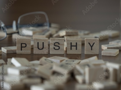 Pushy word or concept represented by wooden letter tiles on a wooden table with glasses and a book