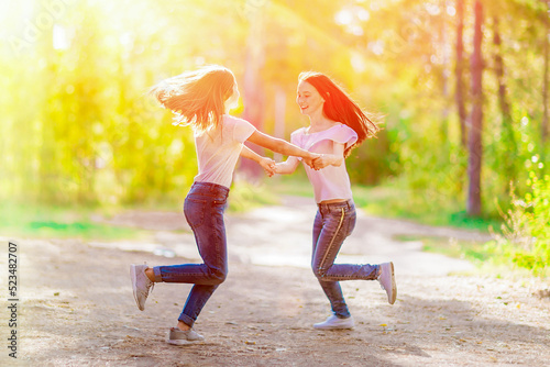 Two cheerful girlfriends are spinning holding hands, on a walk in the summer forest