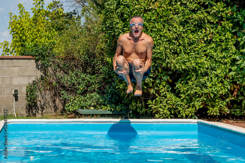 Middle-aged white man with a funny expression dives into the pool with swimming goggles, cannonball style