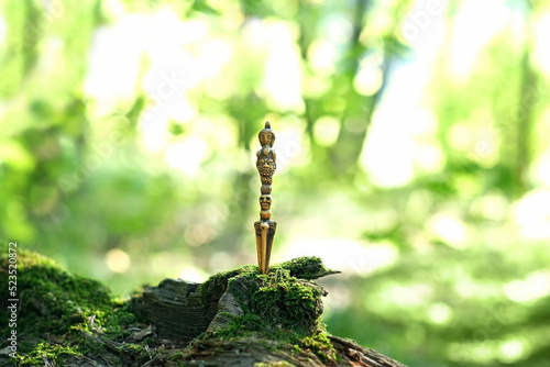 Ritual knife on mossy stump, blurred natural green background. Phurba is a three-sided knife, implement traditionally of Indo-Tibetan Buddhism. used for magic practice, esoteric spiritual ritual