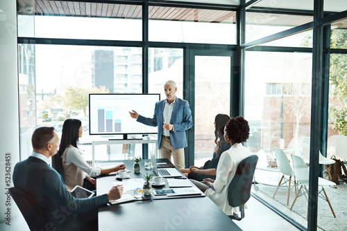 Businesspeople attending a presentation in the boardroom about growth, innovation and development with graphs in a boardroom. Mature man showing great leadership while talking about company vision