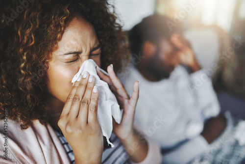 Ill or sick woman with allergy, sinus infection sneezing in tissue or blowing nose during flu season at home. Sick girl caught a bad cold showing symptoms of covid, or suffering from a virus disease