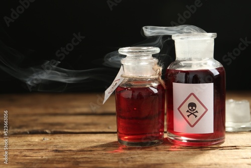 Glass bottles of poison with warning signs on wooden table. Space for text
