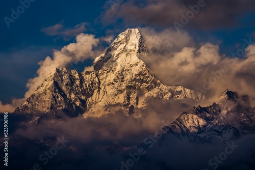 Peak of Ama Dablam mountain in clouds and fog with snow reflecting sunlight