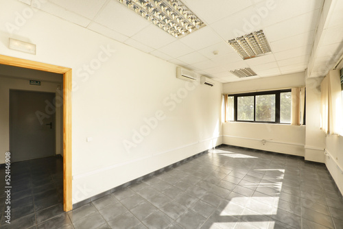 Empty offices with gray stoneware floors, windows on several walls and technical ceilings