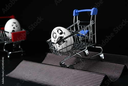 Egg with drawn scared face in shopping cart stunting on black background