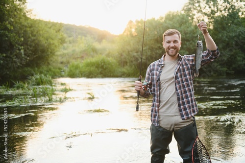 Man with fishing rod, fisherman men in river water outdoor. Catching trout fish in net. Summer fishing hobby