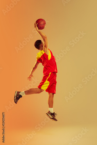 Portrait of young man, basketball player isolated over orange studio background in neon light. Scoring winning goal
