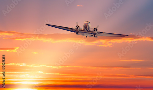 Vintage type old metallic propeller airplane in the sky, sunset clouds with calm sea in the background