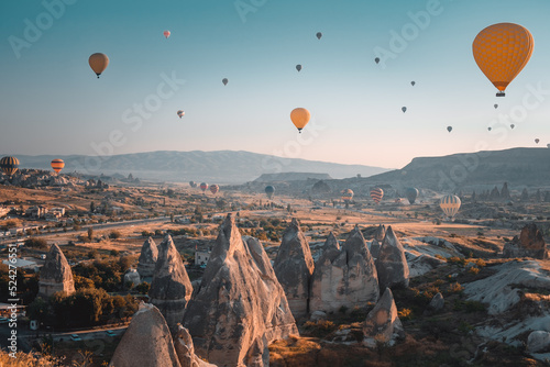Sunrise in Cappadocia - Turkey travel background. Bright hot air balloons fly over cave houses and famous multi head stone mushrooms in Goreme national park. Tourism, holidays, recreation, destination
