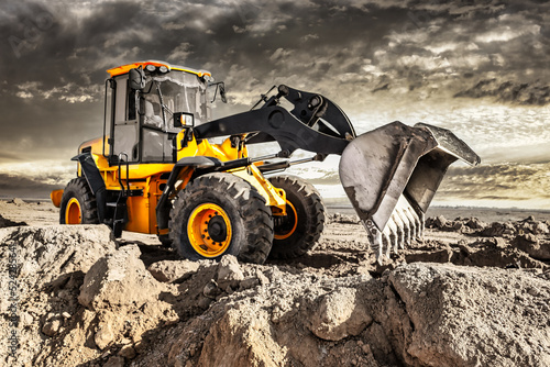 Powerful bulldozer or loader moves the earth at the construction site against the sky. An earthmoving machine is leveling the site. Construction heavy equipment for earthworks.