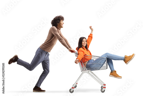 Full length profile shot of a young man running and pushing a girl inside a shopping cart