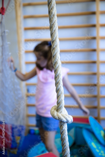 Pretty girl with pigtails playing with the ropes in her school gymnasium.