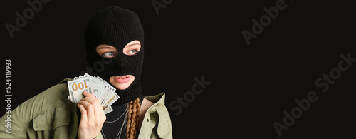 Young woman in balaclava and with money on black background with space for text