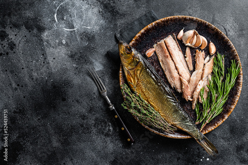 Hot Smoked herring fish fillet on rustic plate with thyme and rosemary. Black background. Top view. Copy space