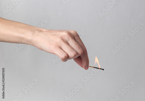 Hand holds a dying match on a gray background