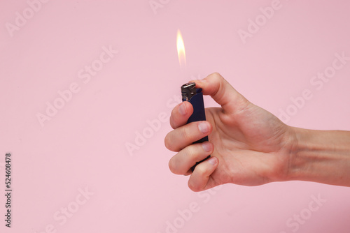 Hand holding a lighter with a flame on a pink background