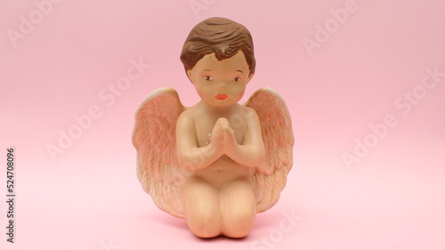 Figura de ceramica de angel orando incado sobre un fondo rosa claro. 