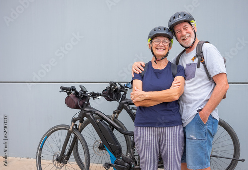 Happy and relaxed senior caucasian couple with helmet enjoying sport activity with electric bicycles in outdoors - sustainable mobility concept