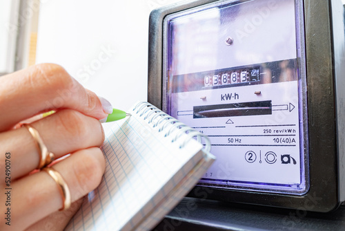 Woman's hands with pen and notepad writes the electricity meter readings at home. Payment of utility services.