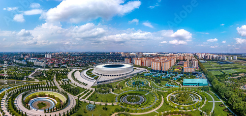 city park in the north-east of Krasnodar (South of Russia) with many round and oval flower beds, photo location objects and a large stadium surrounded by high-rise buildings - aerial panorama