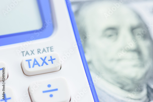 Income and payroll tax calculation, financial concept : TAX button on a calculator and 100 US dollar banknote, depicting a tax calculation that applies to both goods and services at the same tax rate.