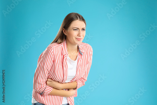 Woman suffering from stomach ache on light blue background, space for text. Food poisoning