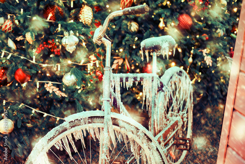 Icy bike on the background of a snow Christmas tree with a bauble near the house, new year