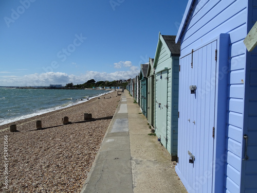 multi-colored beach huts in lee on solent, on the shore, shingle beach and blue green sea, blue sky with few clouds