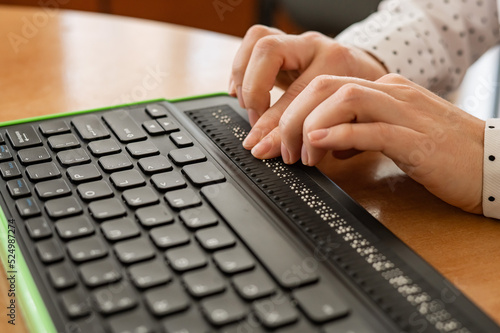 A blind woman uses a computer with a Braille display and a computer keyboard. Inclusive device.