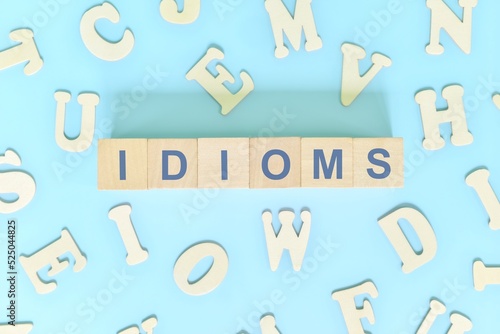 Idioms or idiom concept in English grammar class lesson. Wooden blocks typography flat lay in blue background.