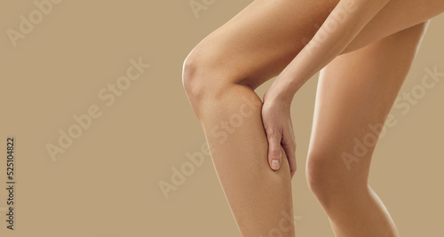 Woman feels a sudden leg cramp and touches her calf. Young lady suffers from pain due to a rare rheumatism symptom or torn, overstretched muscle after overtraining at a gym workout. Copy space banner