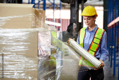 factory worker or warehouser wrapping stretch film parcel on pallet covered cardboard boxed in warehouse storage