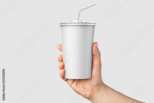 Paper soda cup in a hand with straw mockup template, isolated on light grey background. High resolution.