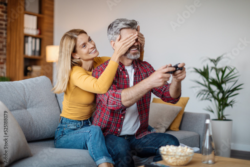 Cheerful mature caucasian lady closes eyes to man with joystick, interferes with online game in free time