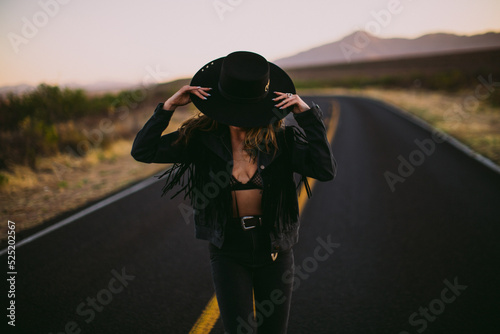 Woman in hat and fringe jacket dancing in the street in the desert at sunset