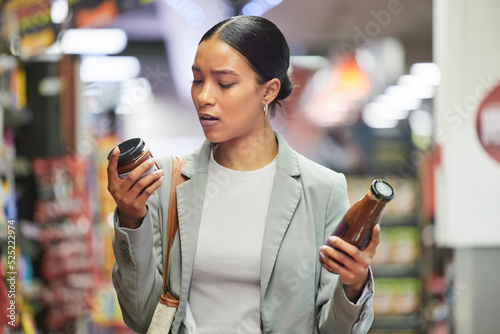 Shopping, retail and customer in a store or supermarket, reading product labels of choice to decide or compare sauce bottles. Consumerism, spending and shopping for food, groceries and a sale offer