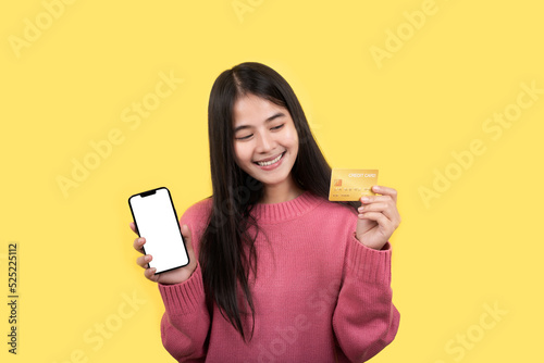 Portrait of a delighted woman standing on a yellow background. holding a cell phone showing a plastic credit card