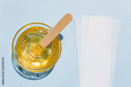 Liquid yellow sugar paste, wooden spatula, depilatory strips on a blue background. Removing unwanted hair. Sugaring. Depilation. Epilation. Beauty. Top view.