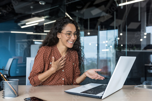 Happy hispanic businesswoman working in modern office using laptop for video call and online meeting with fellow employees, woman smiling and having fun giving a presentation